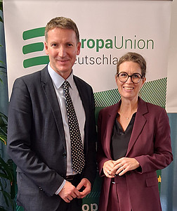 Auf dem Bild sieht man links einen Mann in grauem Anzug und rechts eine Frau im weinroten Hosenanzug vor dem Roll-Up mit dem grünen Logo der Europa-Union Deutschland.